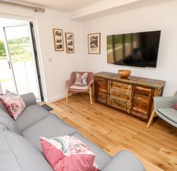 A living room with a gray sofa and two armchairs with cushions a wooden cabinet under a wall-mounted TV and framed pictures on the walls at Claret in Seaview