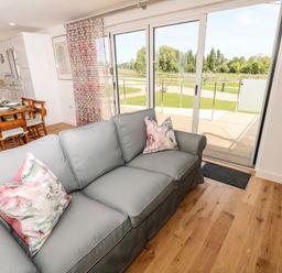 A living room with a gray sofa and floral cushions next to sliding glass doors opening onto a garden at Claret in Seaview