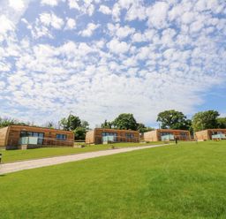 Four wooden small houses on a grassy hill with a path in front of them at Muscat Seaview