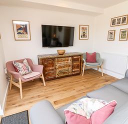 A living room with two armchairs a sofa a wooden cabinet under a wall-mounted television and framed pictures on the walls at Muscat Seaview