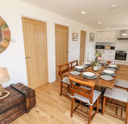 A dining area with a wooden table set with plates and glasses next to a kitchen with white cabinets and three wooden doors at Muscat in Seaview
