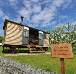 A small wooden cabin on wheels with open doors and steps leading to the entrance in a grassy area with a sign about private parking at Merlot Pondwell near Seaview