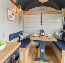 A dining area with a wooden table set for two and blue cushioned bench seating at Malbec Pondwell near Seaview