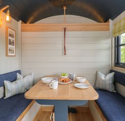 A dining nook with a wooden table and bench seating with cushions bowls cups plates and croissants on table at Malbec Pondwell near Seaview