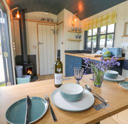 A kitchen with a wooden table set with dishes wine and flowers and a wood stove at Malbec Pondwell near Seaview