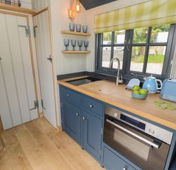 A kitchen with blue cabinets wooden countertop blue kettle and toaster a bowl of green apples and a window with a yellow checked blind at Malbec Pondwell near Seaview