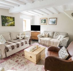 A living room with two beige sofas a brown leather armchair a wooden chest coffee table and a small wooden cabinet with a television at Tan Y Garth Cottage in Glyndyfrdwy near Llangollen
