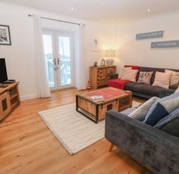 A living room with two sofas a wooden coffee table a media console with a television and glass doors at 8 Pen Llanw Tides Reach in Rhosneigr