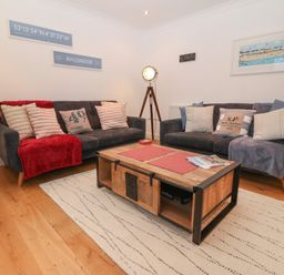 A living room with two sofas a wooden coffee table a floor lamp and wall art at 8 Pen Llanw Tides Reach in Rhosneigr