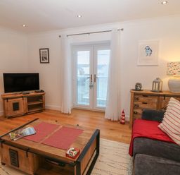 A living room with a sofa a wooden coffee table a TV on a wooden stand and a wooden cabinet with a lamp at 8 Pen Llanw Tides Reach in Rhosneigr