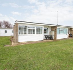 A single story building with patio furniture on a grassy lawn at Chalet 12 in Hemsby