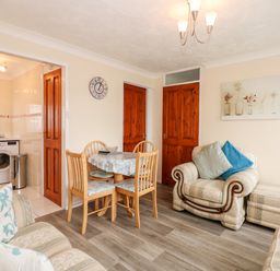 A living room with a dining table and chairs adjacent to a kitchen and armchairs at Chalet 12 in Hemsby