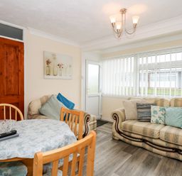 A living room with two sofas a dining table with chairs and a door with windows at Chalet 12 in Hemsby