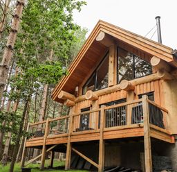 A wooden log cabin with a balcony surrounded by trees at Pine Marten Lodge in Dulnain Bridge near Nethy Bridge