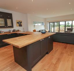 A kitchen and living room with wooden countertops a black sofa and large windows at Shepherds House in Lowick