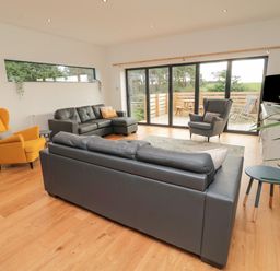 A living room with sofas chairs and a TV next to a large window overlooking a patio at Shepherds House in Lowick