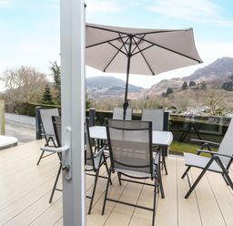 A patio with a table and six chairs under an umbrella overlooking hills at Red Kite Lodge in St Fillans