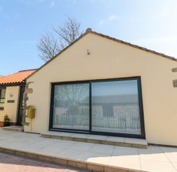 A bungalow with large sliding glass doors and a tiled roof at 3 The Paddock in Benthall near Beadnell