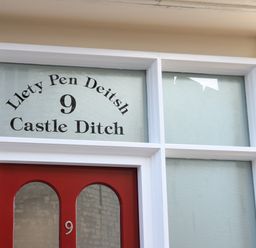 A red door with windows above displaying the text Llety Pen Deitsh 9 Castle Ditch at Llety Pen Deitsh 1 in Caernarfon