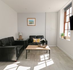 A living room with two black sofas a wooden coffee table a side table with a lamp a wall cabinet a window with plants and a wall-mounted TV at Llety Pen Deitsh 1 in Caernarfon
