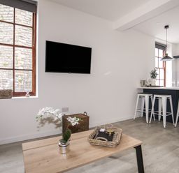 A living area with a wooden coffee table and TV mounted on the wall next to a kitchen island with stools at Llety Pen Deitsh 1 Caernarfon