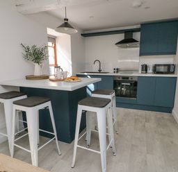 A modern kitchen with blue cabinets a white countertop an island with stools and a window at Llety Pen Deitsh 2 in Caernarfon