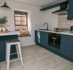 A kitchen with blue cabinets a black sink a window with cushions and two stools at Llety Pen Deitsh 2 in Caernarfon