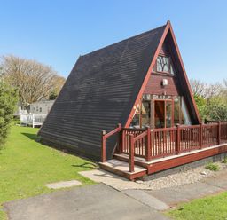 An A-frame cabin with a wooden deck surrounded by grass and trees at 171 Snowdonia View in Chwilog