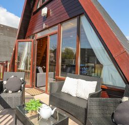 An outdoor patio with black wicker chairs and sofa with cushions a glass table a teapot and plant outside an a frame building at 171 Snowdonia View in Chwilog