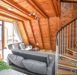 A living area with wooden walls and ceiling featuring a gray sofa set and a spiral staircase at 171 Snowdonia View in Chwilog