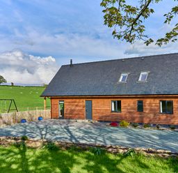 A wooden house with a pitched roof and skylights in a rural area with a gravel driveway and a swing set at Holly Lodge in Forden near Montgomery
