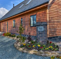 A wooden house with a garden bed and a brick pillar with a sign reading Holly Lodge in Forden near Montgomery