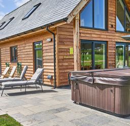 An outdoor patio area with lounge chairs and a covered hot tub next to a wooden house at Holly Lodge in Forden near Montgomery