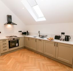 A kitchen with beige cabinets a built-in oven gas stove microwave and skylight at Sgubor in Llangefni