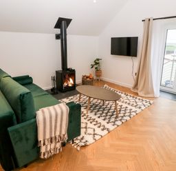 A living room with a green sofa a wood stove a mounted TV a coffee table and glass doors at Sgubor in Llangefni