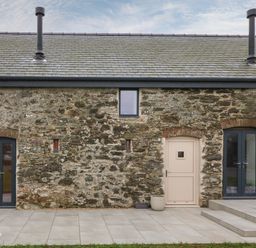 Exterior view of a stone building with a beige door and two dark gray French doors at Beudy in Llangefni