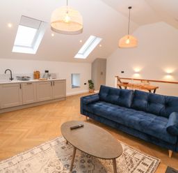An open plan living space with a blue sofa wooden coffee table kitchen cabinets and dining table with chairs at Beudy in Llangefni