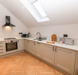 A kitchen with light grey cabinets and wooden floor under a skylight at Beudy in Llangefni
