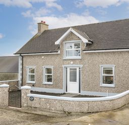 A pebble dash house with a white door three windows a slate roof and a low surrounding wall at Grannys in Bushmills County Antrim