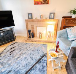A living room with a television on a stand a tiled fireplace with decorations a blue armchair and a small table with snacks and wine at Grannys in Bushmills County Antrim