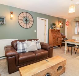 A living room with a brown leather sofa and a wooden coffee table and a dining table with chairs at Cwm Caeth Cottage in Nantmor near Beddgelert