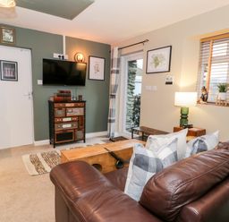 A living room with a brown leather sofa pillows a wooden chest and a TV on the wall at Cwm Caeth Cottage in Nantmor near Beddgelert