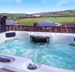 An outdoor hot tub with water jets and headrests overlooking green fields and rooftops at Chi Prenn Byhan in Tintagel