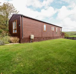 A wooden mobile home on a grass lawn with trees and fields in the background at Orchard View in Bossiney near Tintagel