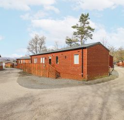 A row of wooden holiday lodges along a gravel road with trees in the background at Windermere View in Pony Meadow 37 White Cross Bay near Windermere