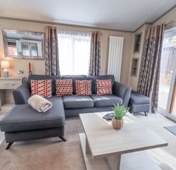 A living room with a gray sectional sofa and patterned cushions a wooden coffee table and large windows at Windermere View in Pony Meadow 37 White Cross Bay near Windermere