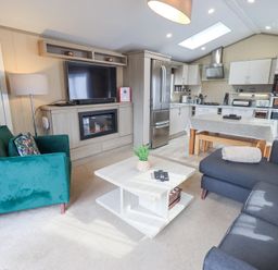 A living room and kitchen with a green armchair a black sofa a coffee table a TV above an electric fireplace and a dining table at Windermere View Pony Meadow 37 White Cross Bay near Windermere