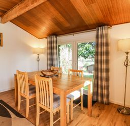 A dining area with a wooden table and four chairs next to large glass doors with plaid curtains at Stonewood Lodge in Woolsery