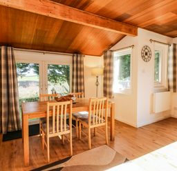 A dining area with a wooden table and four chairs near windows with plaid curtains at Stonewood Lodge in Woolsery