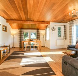 A living room with a wooden ceiling a dining table with chairs a television and a sofa at Stonewood Lodge in Woolsery